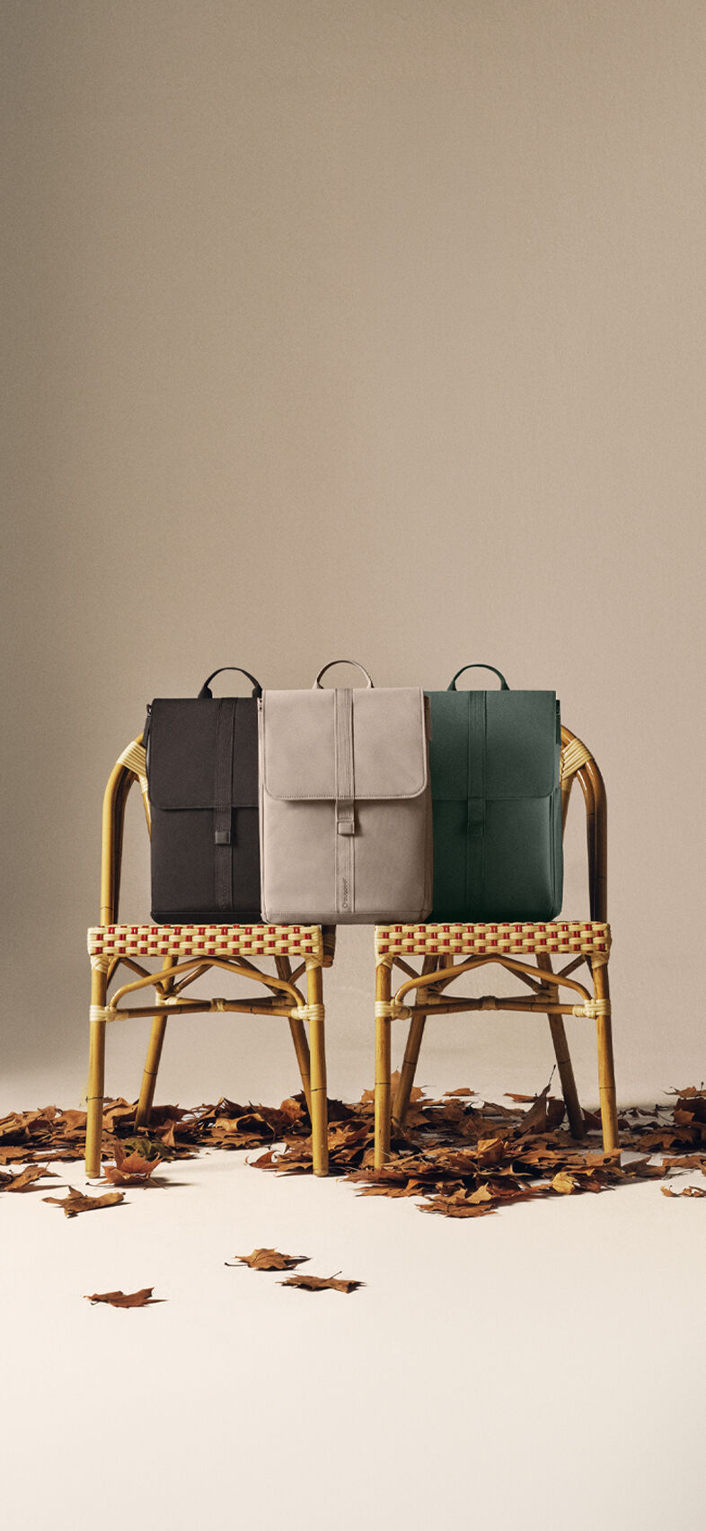 Three Bugaboo changing backpacks in autumn colors sit on two rattan chairs beneath an old street lamp, with scattered leaves on the ground.