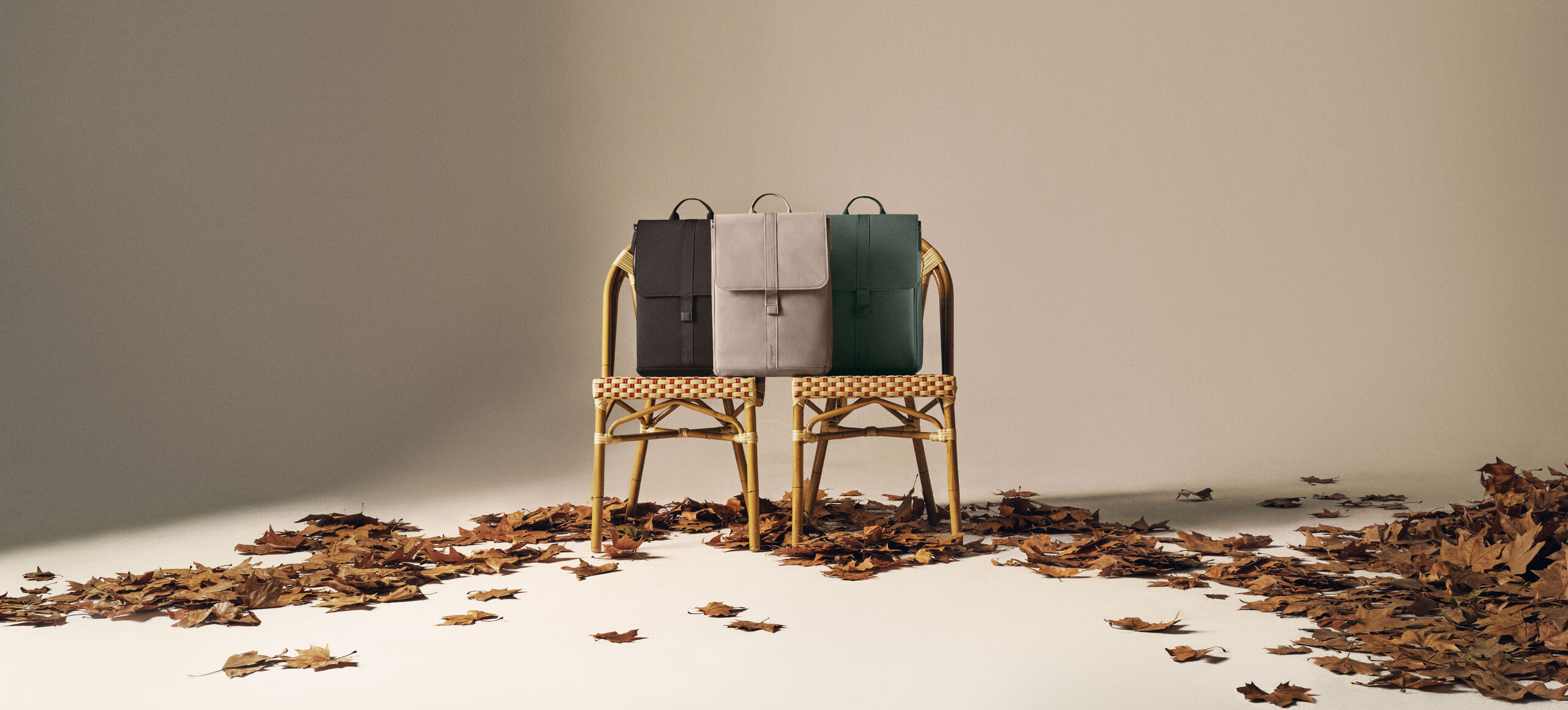 Three Bugaboo changing backpacks in autumn colors sit on two rattan chairs beneath an old street lamp, with scattered leaves on the ground.