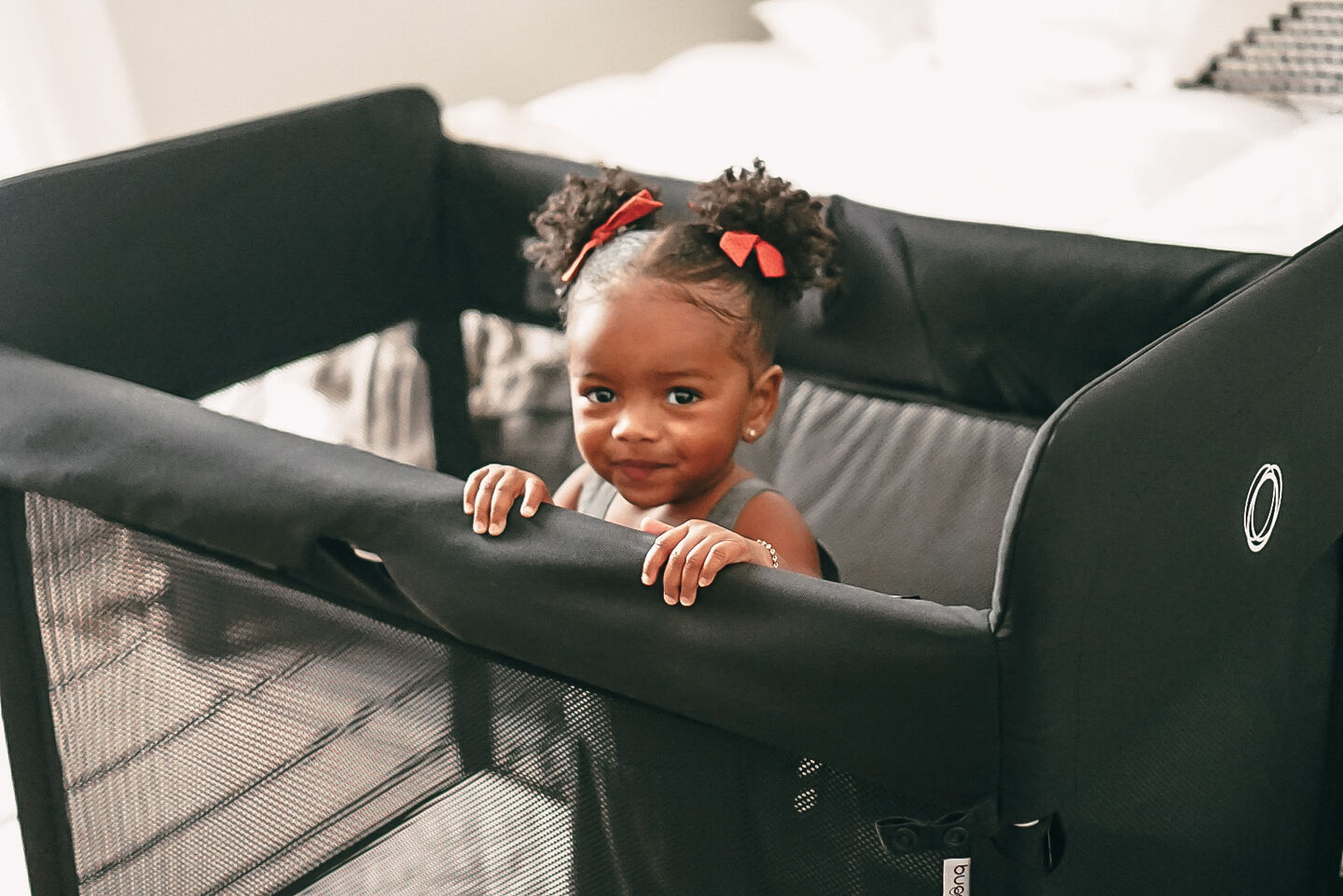 A toddler with her hair in bunches peeking over the edge of the Bugaboo Stardust travel cot.