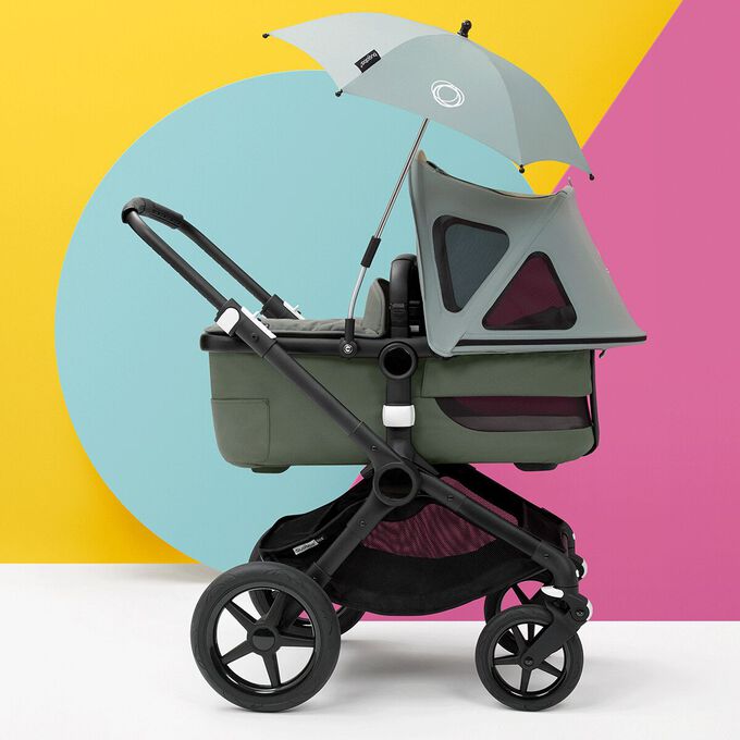 A Bugaboo Fox with breezy sun canopy and parasol, all in green fabrics, inside a colorful studio.