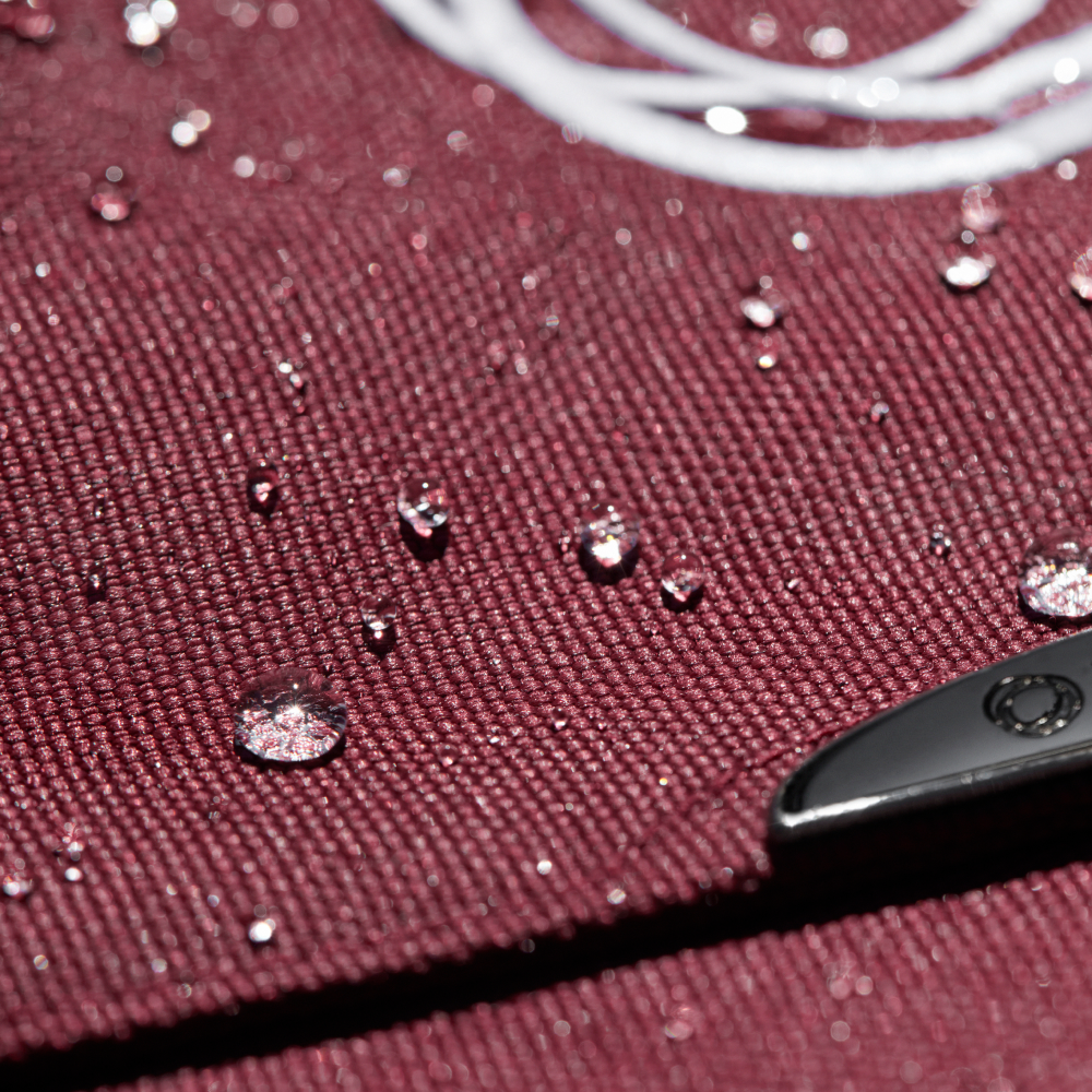 Close-up van waterdruppels van de Dark Cherry bekleding van een Bugaboo parelen, wat wijst op waterafstotend materiaal.