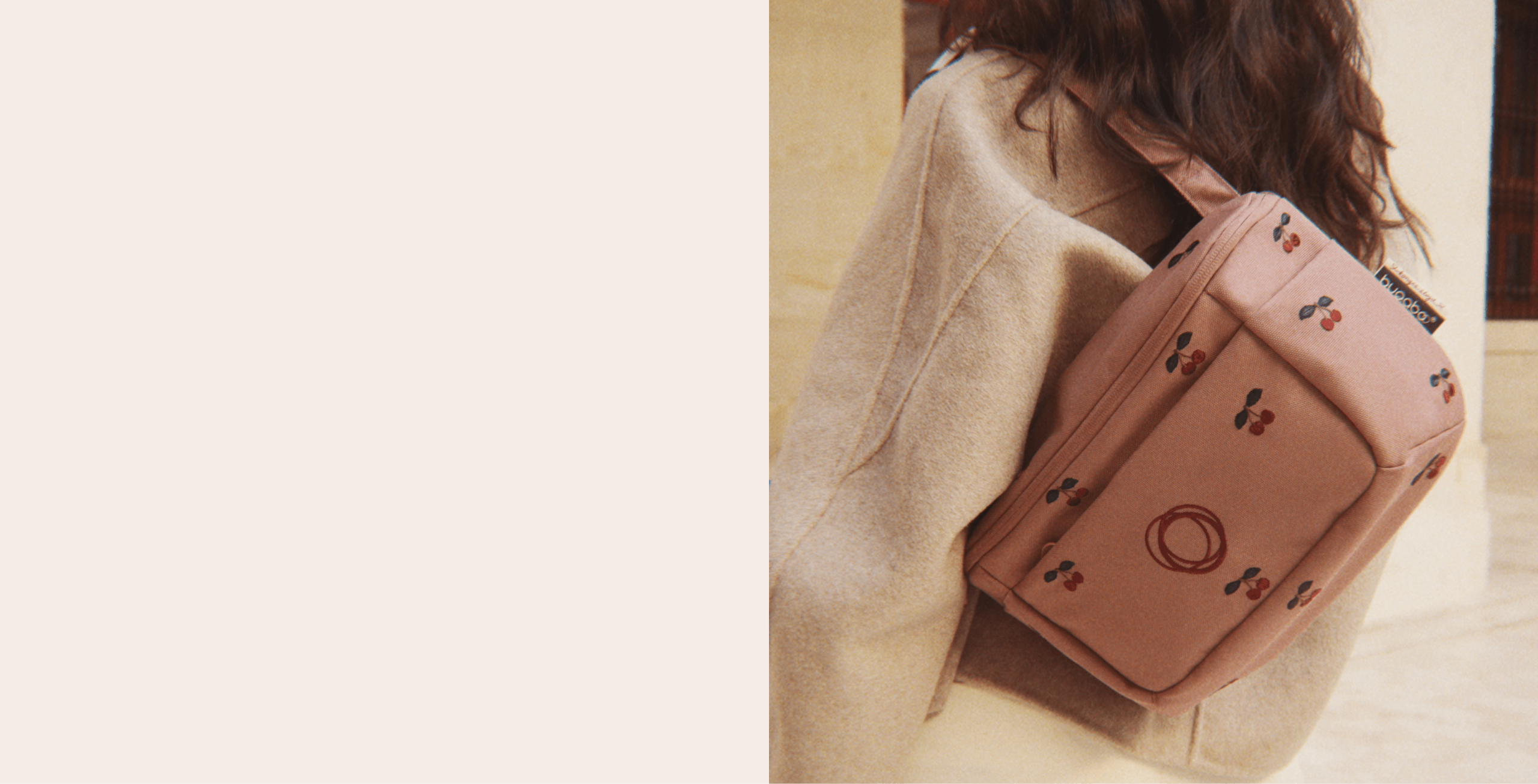 A close up of a Bugaboo x Konges Sløjd Limited Edition organizer, with cherry patterns embroidered on Dusty Pink fabric, worn over a beige coat.