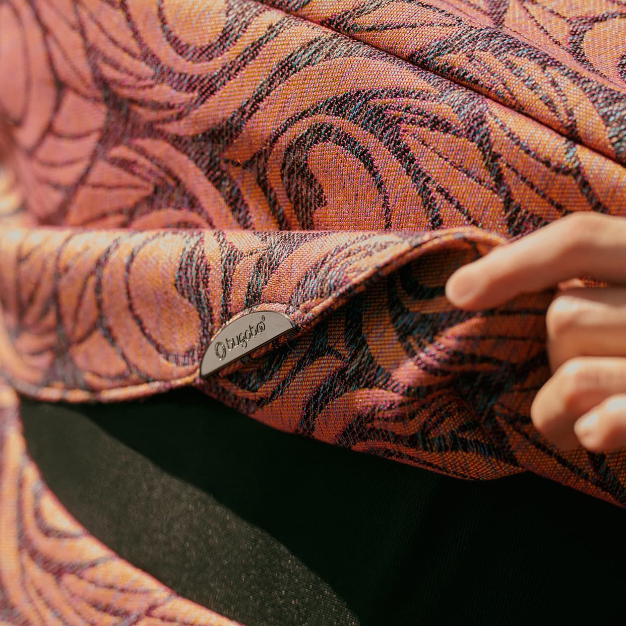 A hand lifts up the flap of a Bugaboo X Artipoppe Limited Edition sun canopy. The canopy features an Argus motif in iridescent golden-purple.