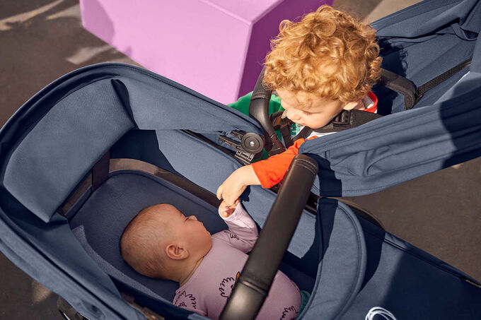 Little boy holds his little sister’s hand while she sleeps in their double stroller