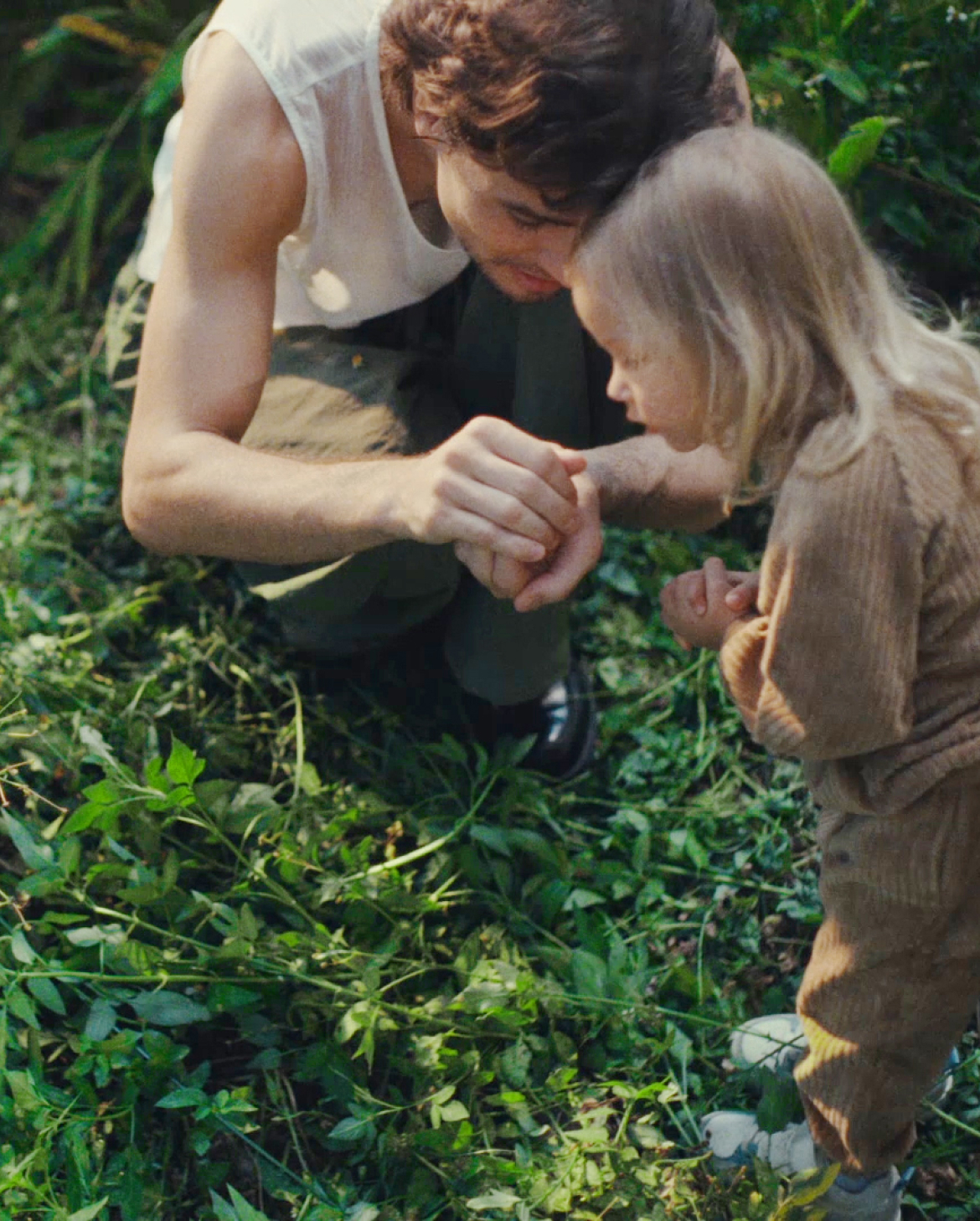 아빠와 딸이 풀이 무성하게 자란 정원에 웅크리고 앉아 있습니다. 아빠는 손에 잡은 무언가를 딸에게 보여주고 있습니다. 