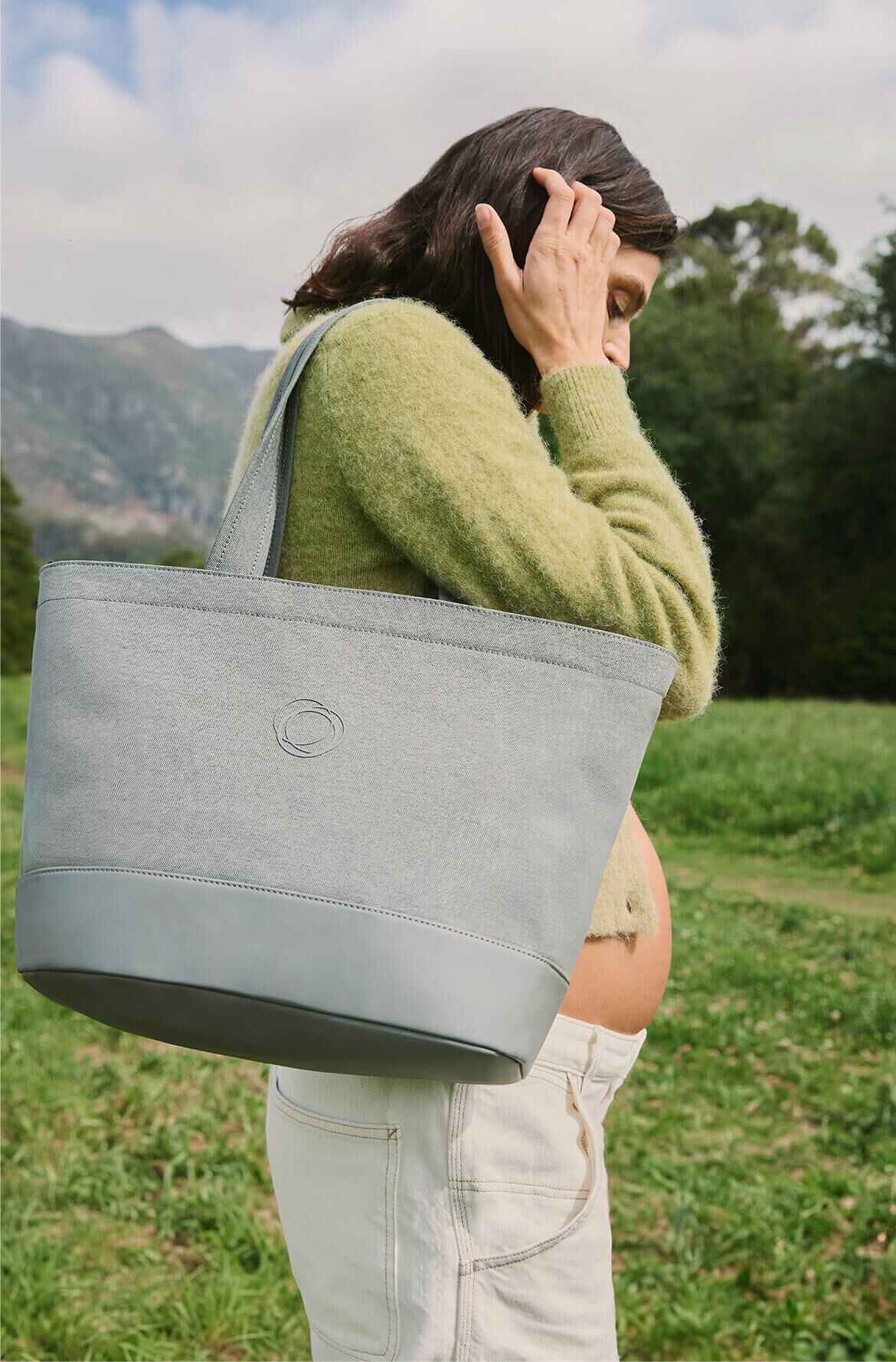A pregnant woman walks through a nature park with a Bugaboo organizer bag slung over her shoulder.