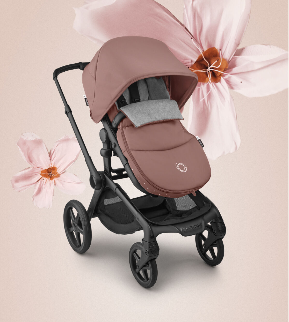 A Bugaboo stroller decked out with with Dusty Pink sun canopy and footmuff is displayed in front of a soft pink background with large cherry blossoms.