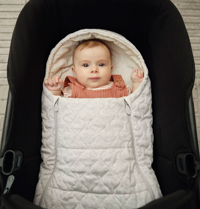 Un bebé acurrucado de forma segura en un saco de recién nacido Bugaboo de color blanco.