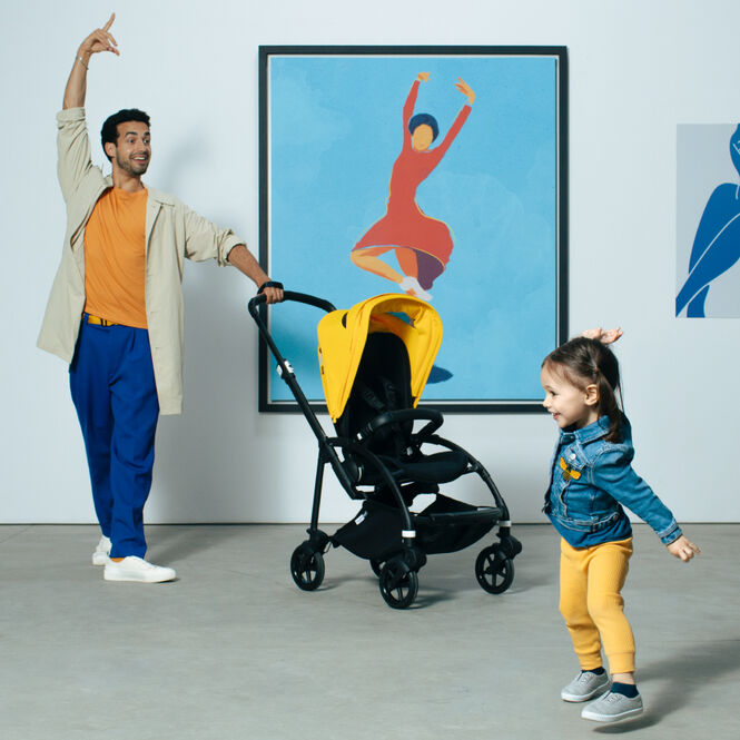 Dad and daughter dancing quirkily inside an art gallery; Dad is holding onto a Bee 6 stroller.