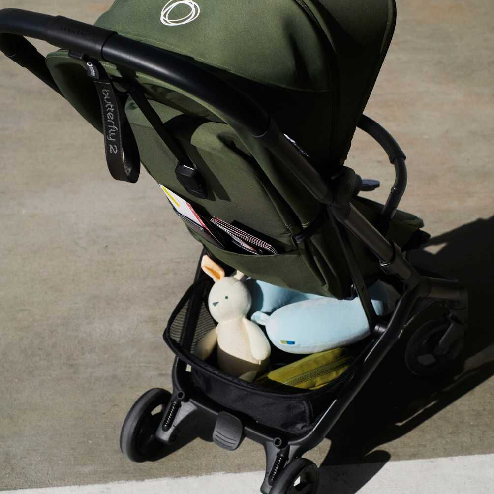 Vue arrière de la poussette ultra compacte Bugaboo Butterfly 2. Le panier sous siège est rempli à ras bord de jouets et de produits essentiels pour bébé.