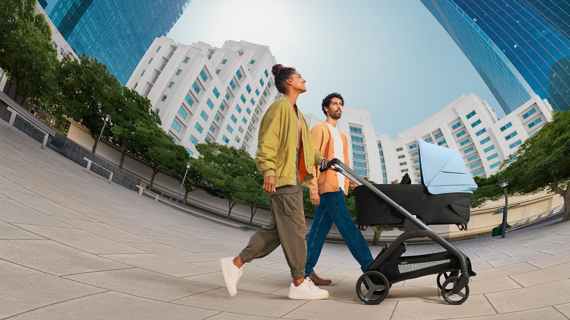 Promenade citadine pour ce couple au guidon de la poussette siège Bugaboo Dragonfly. Poussette jaune à capote extensible avec panneaux de ventilation spéciaux.