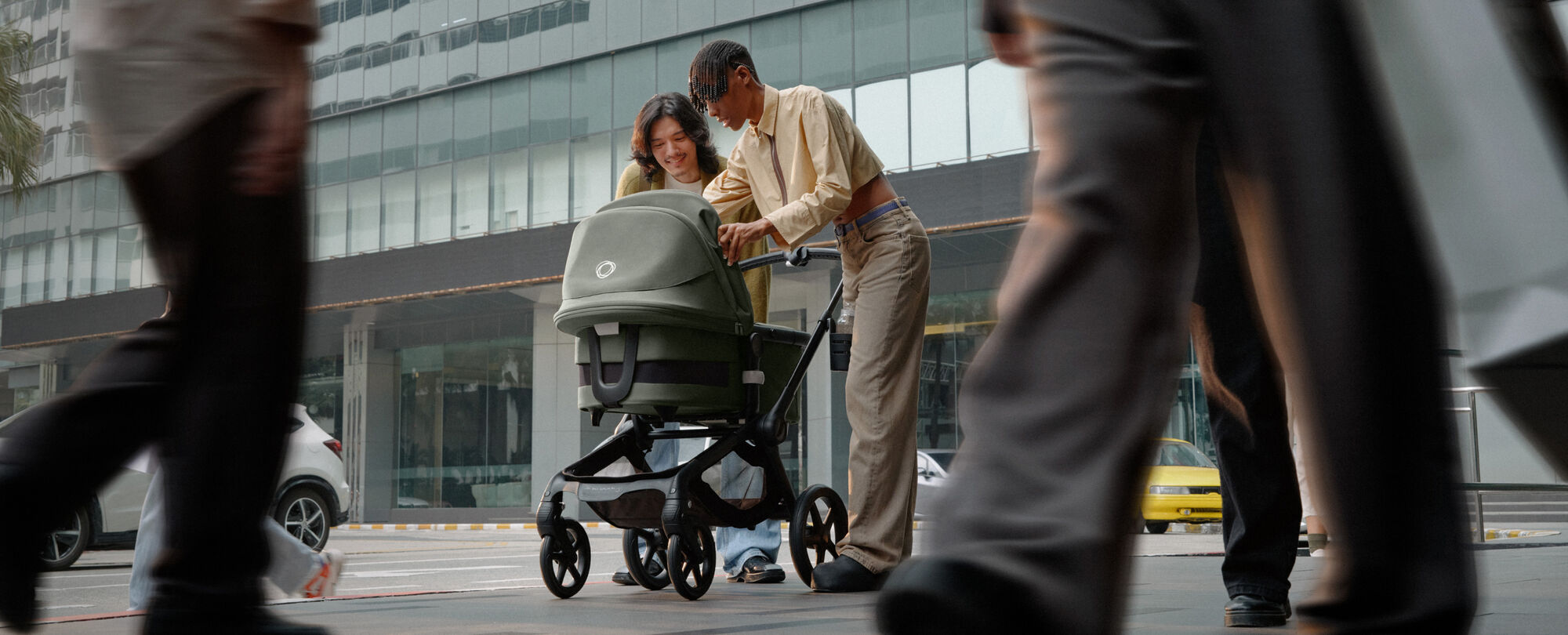 Twee ouders staan in een drukke straat en lachen naar hun baby in een Bugaboo Fox 5 kinderwagen.