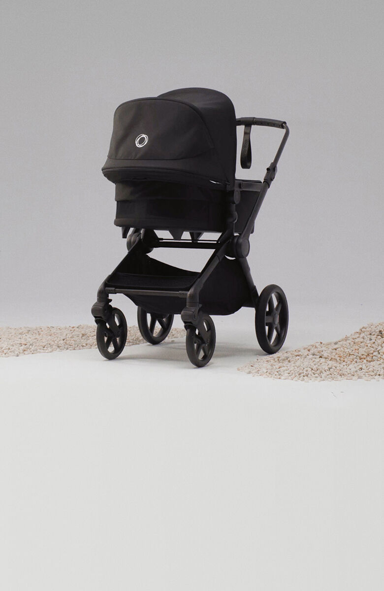 A Bugaboo Cub all-terrain stroller in black fabrics inside a studio space, next to piles of sand on the ground.