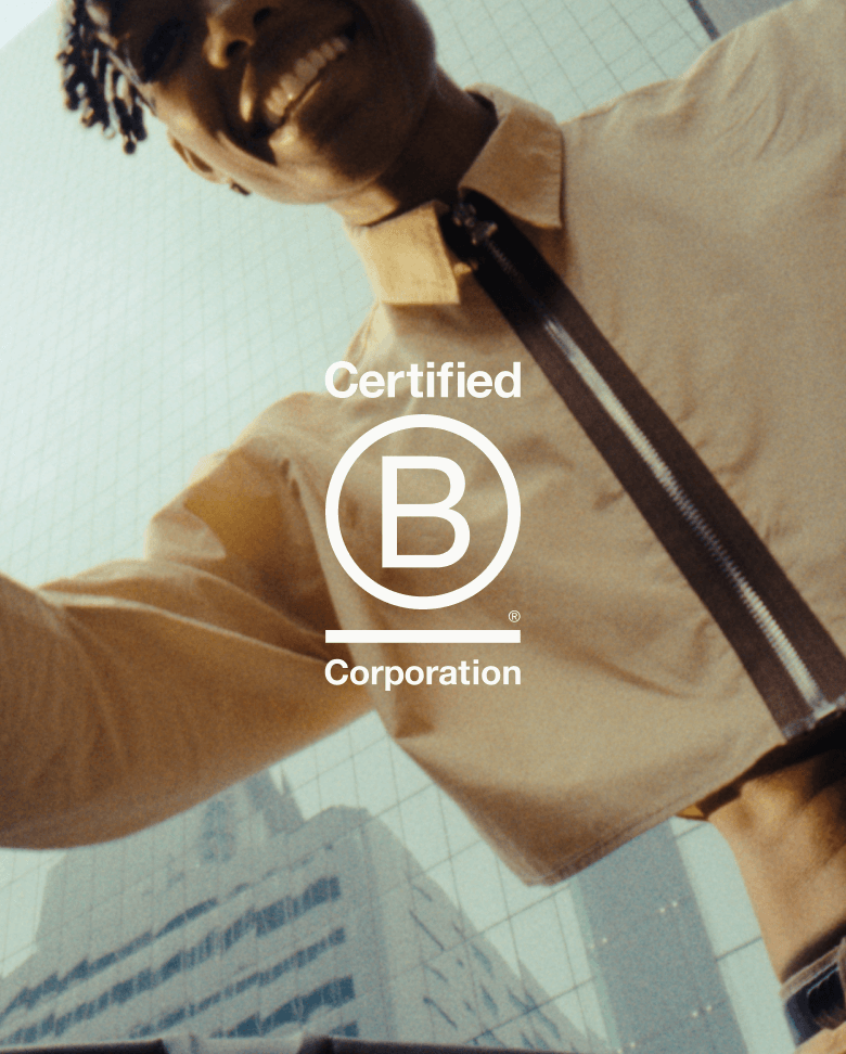 Point of view from a stroller looking up. A dad is looking down at his baby, smiling in happiness. Behind him are tall glass buildings. The B Corp logo sits in the middle of the picture.