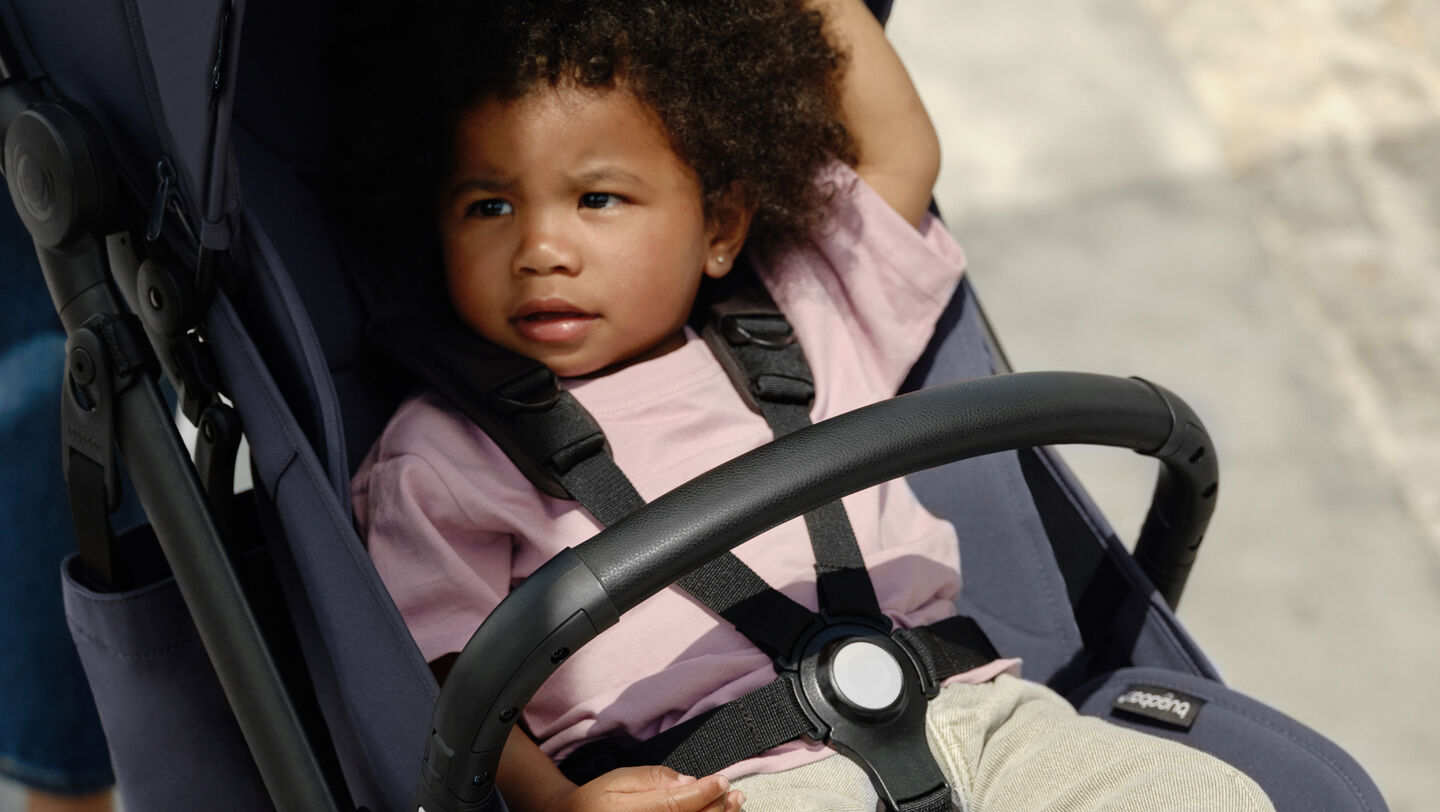 Ein Kleinkind, das sicher im 5-Punkt-Gurt eines Bugaboo Kompaktkinderwagens gesichert ist.