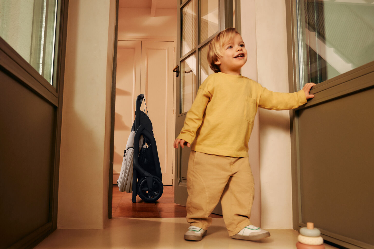 Compact folded Bugaboo stroller standing self-upright in a hallway next to a smiling toddler