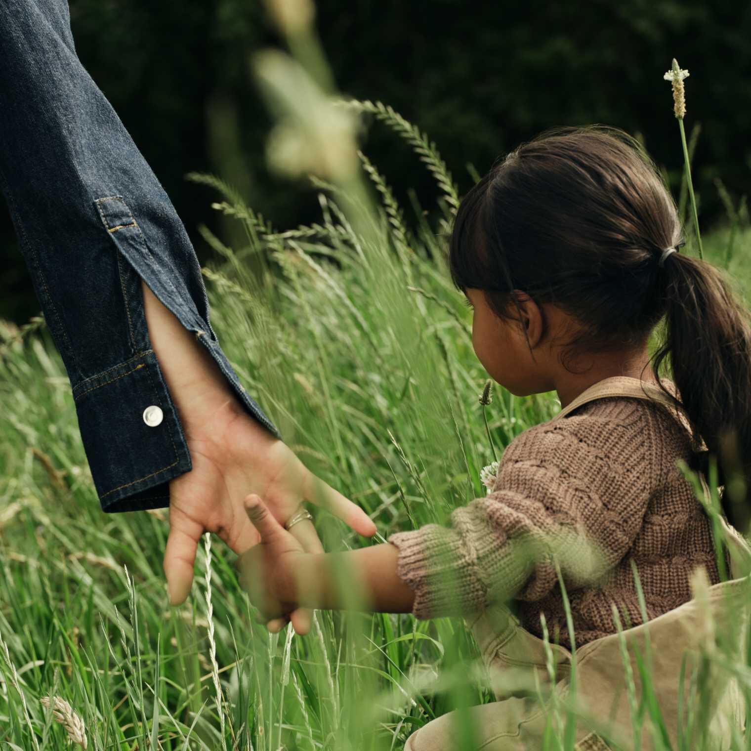 Une petite fille et sa maman se promènent main dans la main dans l'herbe haute.