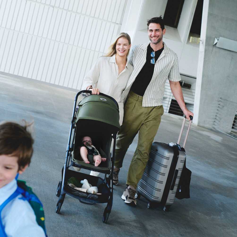Un couple au sourire radieux s'apprête à partir en voyage. La maman pousse une poussette Bugaboo Butterfly 2 où se trouve son bébé, tandis que le papa tire une grande valise à roulettes.