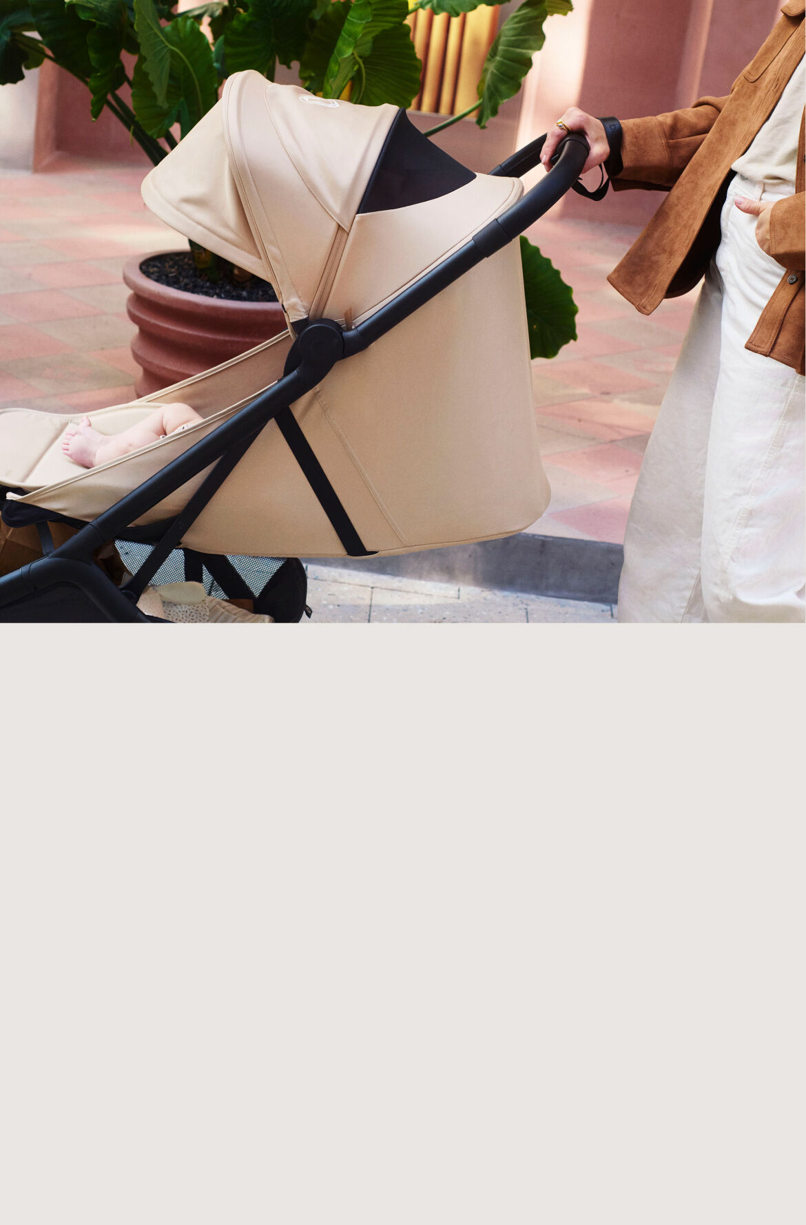 Mom strolls with baby in a Bugaboo Butterfly 2 Plus travel pram in Desert Taupe fabrics. The pram seat lays flat.
