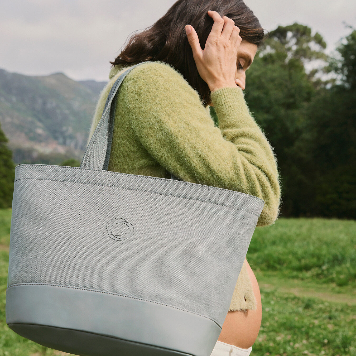 A pregnant woman walks through a nature park with a Bugaboo organizer bag slung over her shoulder.