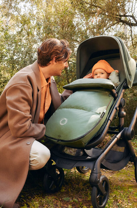 A parent pushes a Bugaboo Fox 5 Renew bassinet stroller with a Bugaboo wheeled board attached, while a child walks alongside.