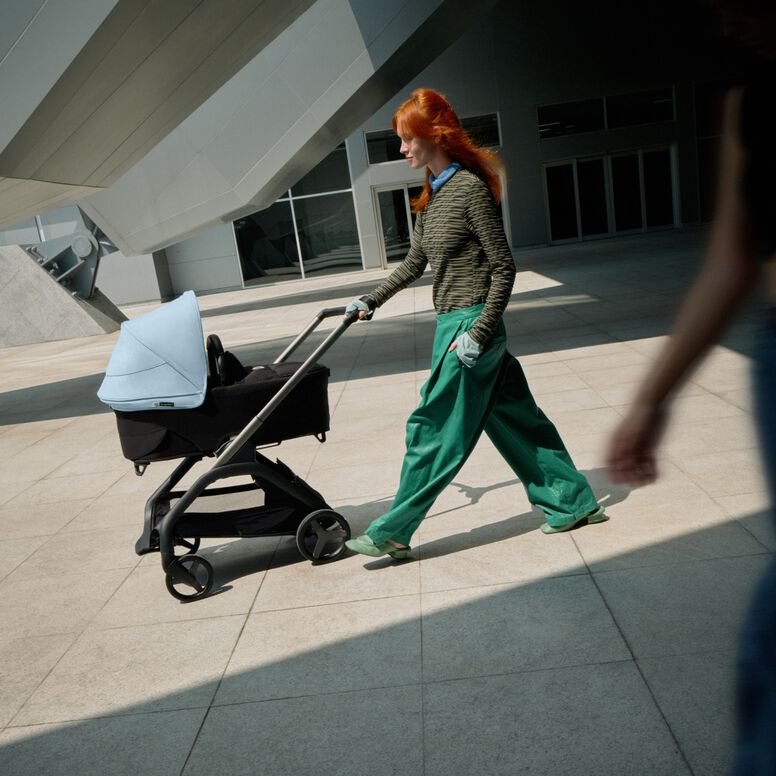 A confident mom walks with her baby in a Bugaboo Dragonfly city stroller as she glides past a futuristic building.
