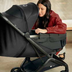 A mother leans over to look inside a Bugaboo baby nest on a Bugaboo Butterfly 2 travel pushchair with black fabrics.