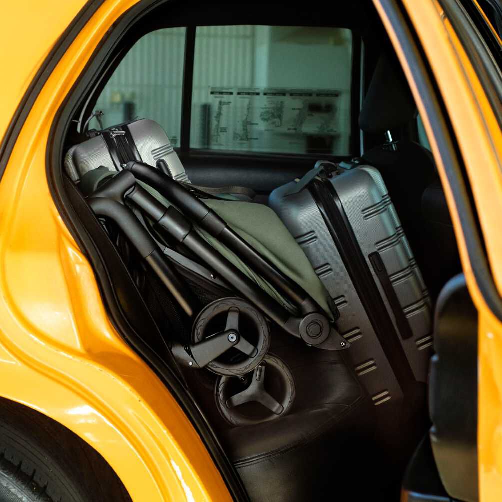 Une poussette Bugaboo Butterfly 2 repliée est rangée sur la banquette arrière d'une voiture jaune de manière compacte, avec d'autres bagages.