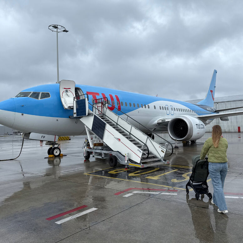 A mom pushes a Bugaboo Butterfly 2 travel stroller towards the boarding stairs of a TUI airplane on the tarmac.