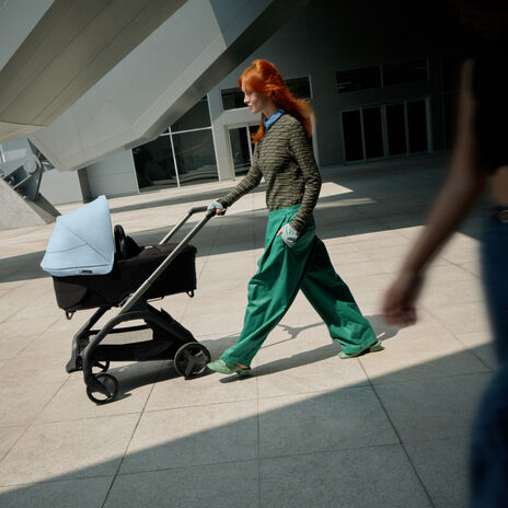 A confident mom walks with her baby in a Bugaboo Dragonfly city stroller as she glides past a futuristic building.