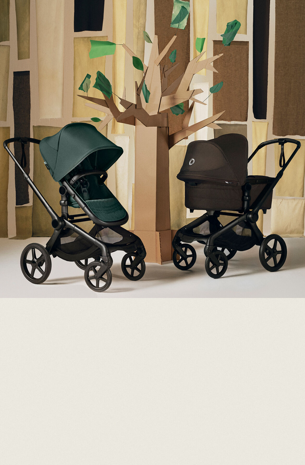 Ein Bugaboo Fox 5 Renew Kinderwagen mit Sitz in Fern Green und ein Bugaboo Fox 5 Renew Kinderwagen mit Liegewanne in Cocoa Brown. Sie stehen in einer stilisierten Innenkulisse mit einem Baum aus Pappe und abstrakten Gebäudeformen.