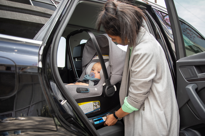 A baby sitting in Bugaboo Turtle Air by Nuna car seat, which is being adjusted by a woman wearing a grey coat