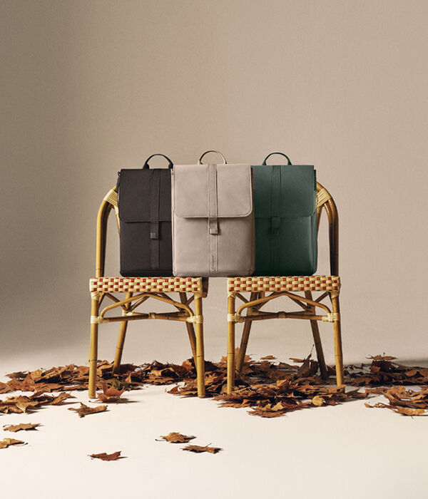 Three Bugaboo changing backpacks in autumn colors sit on two rattan chairs, with scattered leaves on the ground.
