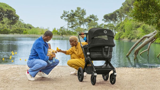 Smiling couple with their baby and stroller by a lake with trees and ducks