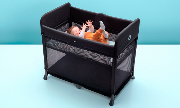 A baby in an orange rumper lying in the bassinet insert of the Bugaboo Stardust travel cot.