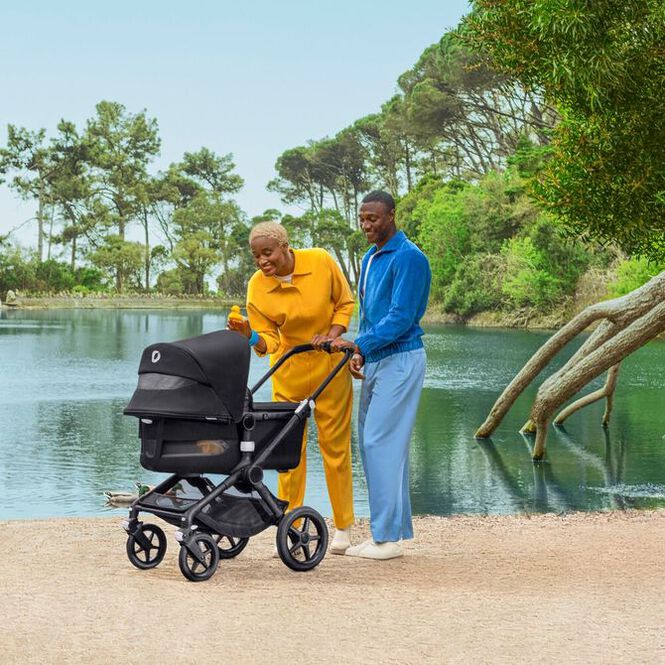 Mom and Dad smiling at an out of sight baby in a Fox 3 stroller, behind them is a beautiful lake.