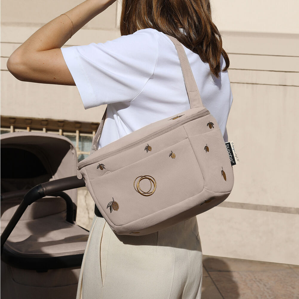 A mother carries a Bugaboo X Konges Sløjd Limited Edition organizer on her shoulder. The organizer features Konges Sløjd's signature lemon print.