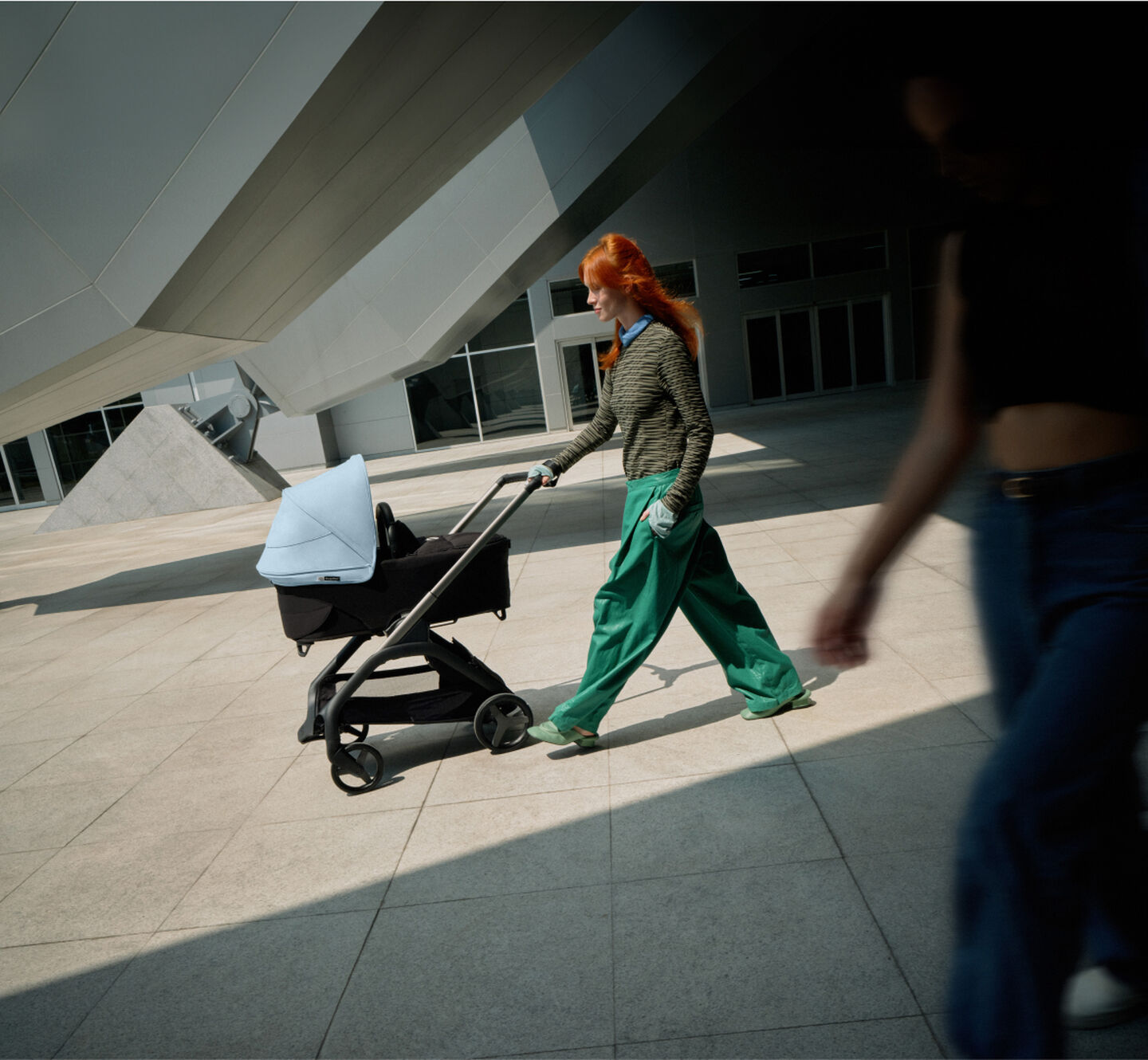 Een zelfverzekerde moeder loopt met haar baby in een Bugaboo Dragonfly urban kinderwagen langs een futuristisch gebouw.