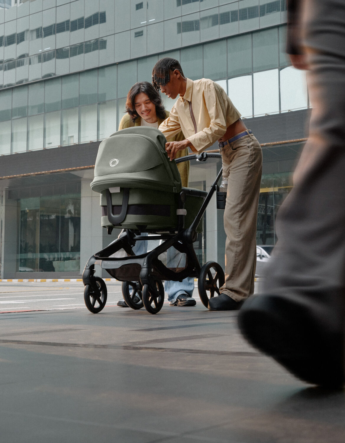 Twee ouders staan in een drukke straat en lachen naar hun baby in een Bugaboo Fox 5 kinderwagen.