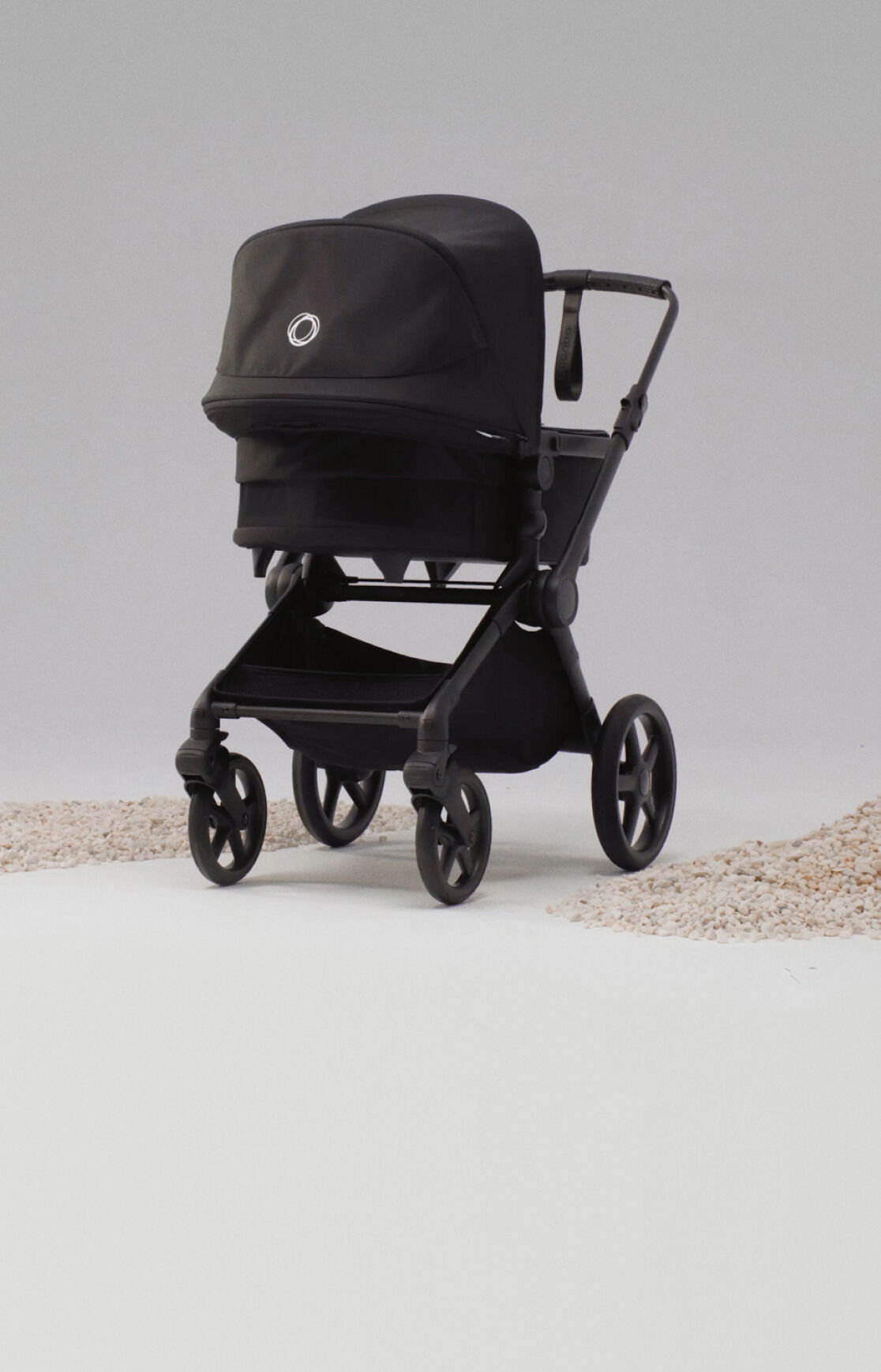 A Bugaboo Cub all-terrain pushchair in black fabrics inside a studio space, next to piles of sand on the ground.