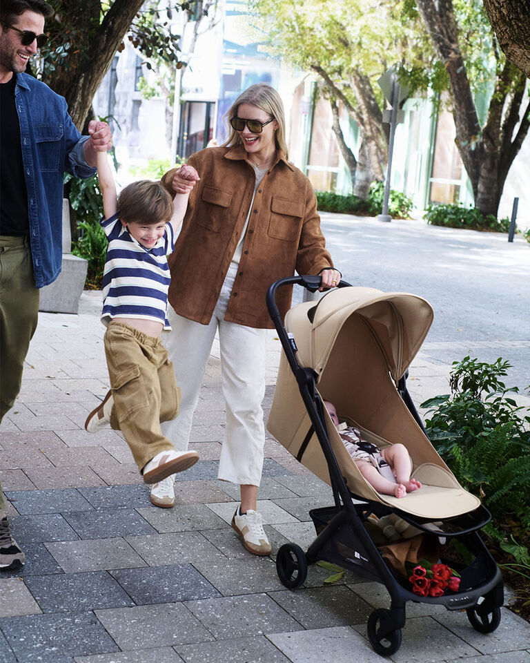 A dad carries his child in one arm and the Bugaboo Butterfly 2 travel stroller over his shoulder, while standing on a moving escalator.