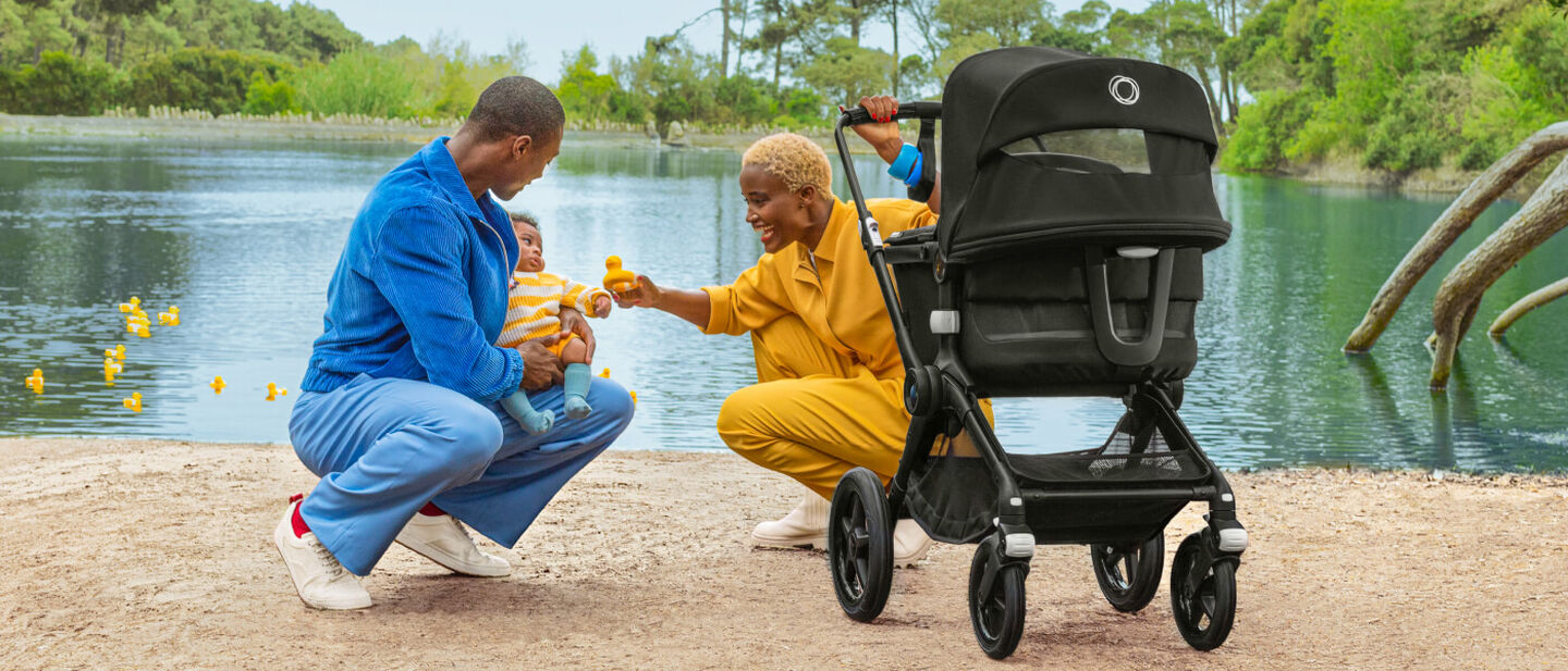Parents playing with baby beside a lake with a Bugaboo Fox 3 stroller next to them.