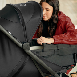 A mother leans over to look inside a Bugaboo baby nest on a Bugaboo Butterfly 2 travel pushchair with black fabrics.