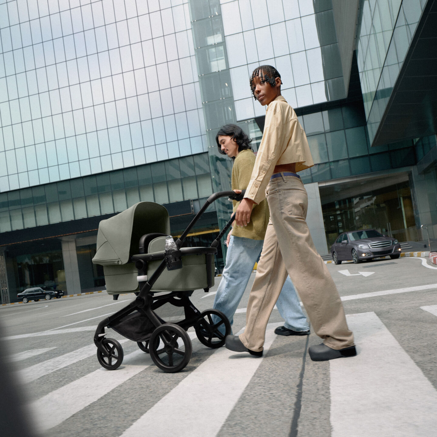 A stylish couple take confident strides with their newborn in a Bugaboo Fox 5 stroller. They're surrounded by glass skyscrapers.