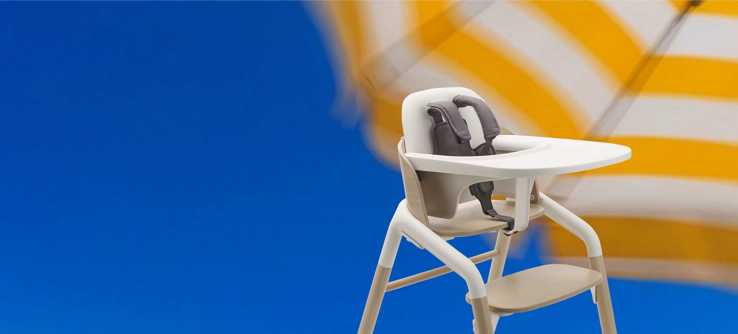 A blurred close-up of yellow and white striped beach umbrellas against a bright blue sky. With a Bugaboo Giraffe in the middle.