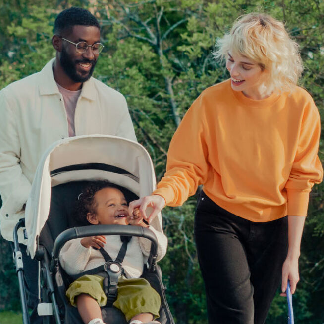 Mom and Dad taking baby in a Bugaboo stroller out for a walk in the park.