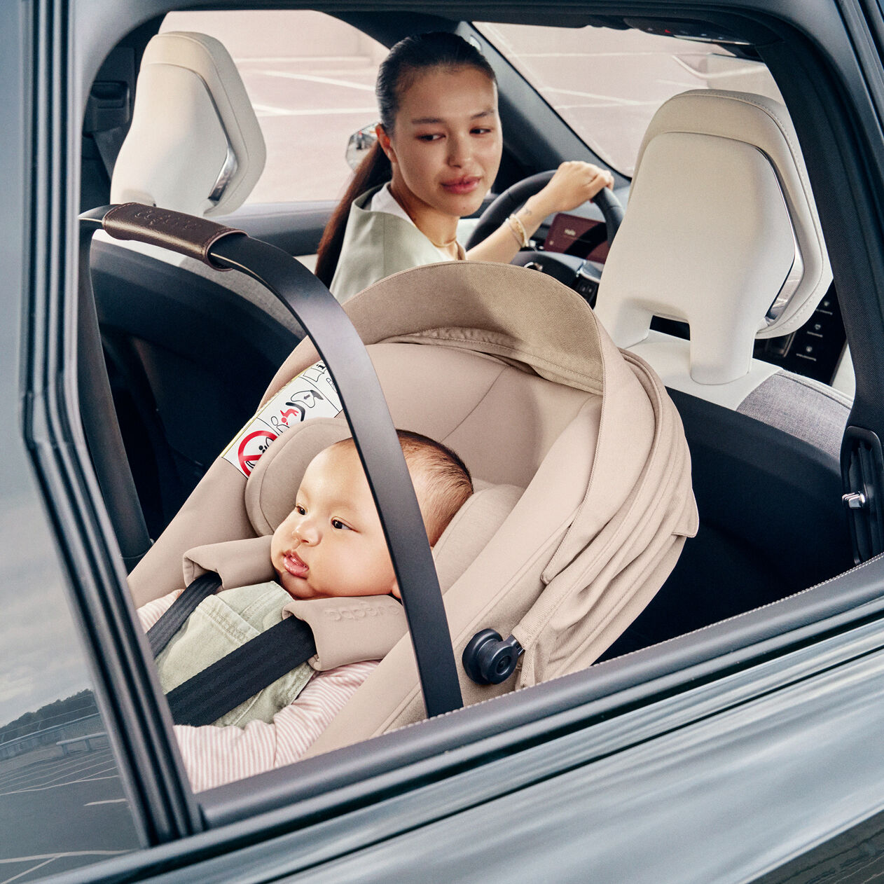 Une maman au volant jette un coup d'œil à son bébé installé dos à la route dans le siège-auto i-Size Bugaboo Otter by Nuna.