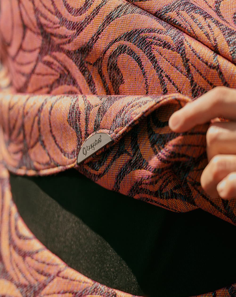 A hand lifts up the flap of a Bugaboo X Artipoppe Limited Edition sun canopy. The canopy features an Argus motif in iridescent golden-purple.