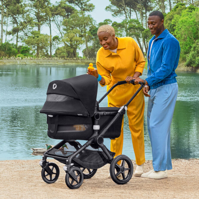 Mom and Dad smiling at an out of sight baby in a Fox 3 stroller, behind them is a beautiful lake.