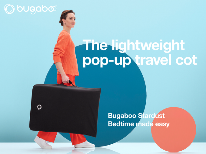 Woman in matching orange top and trousers holding the Bugaboo Stardust in its black travel case. Text reads: ‘The lightweight pop-up travel cot. Bugaboo Stardust: bedtime made easy’.